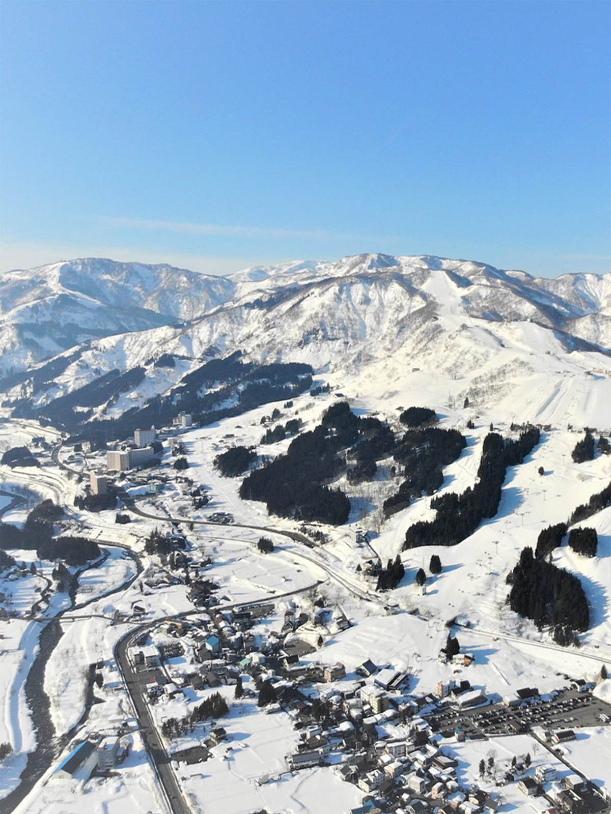 Aerial view over Ishiuchi Maruyama's groomed ski runs and the town of Ishiuchi, Niigata, with the Uonuma mountains beyond