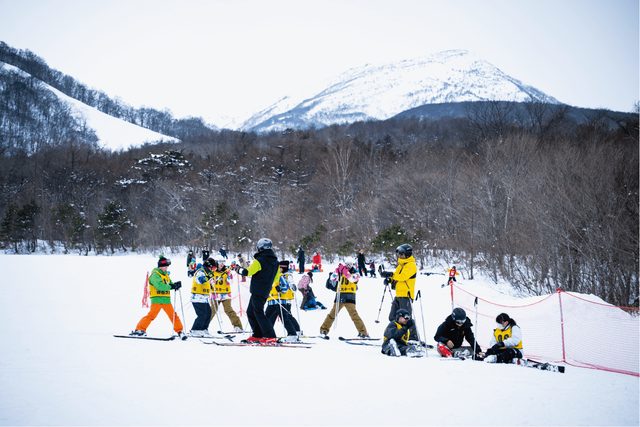 Young ski racers in bibs at the foot of the course at Miyagi Zao Shiroishi, with the snow-covered Zao peaks behind