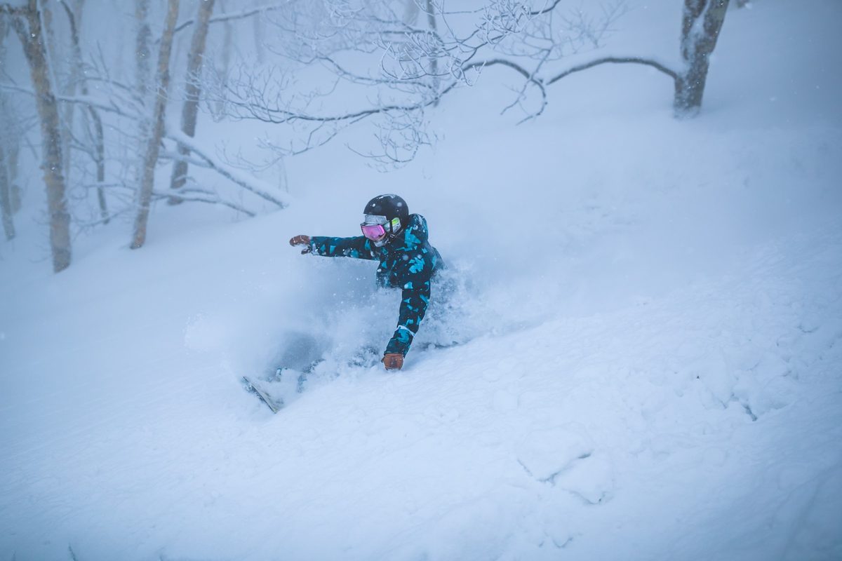 A snowboarder riding deep powder through frosted trees at Ryuoo Ski Park, Nagano
